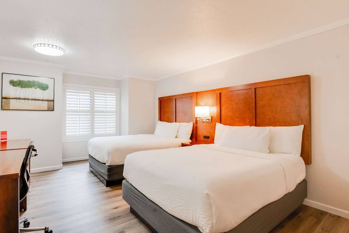 Ett hotellrum med två sängar, ett skrivbord, en stol, en lampa och en tavla på väggen.