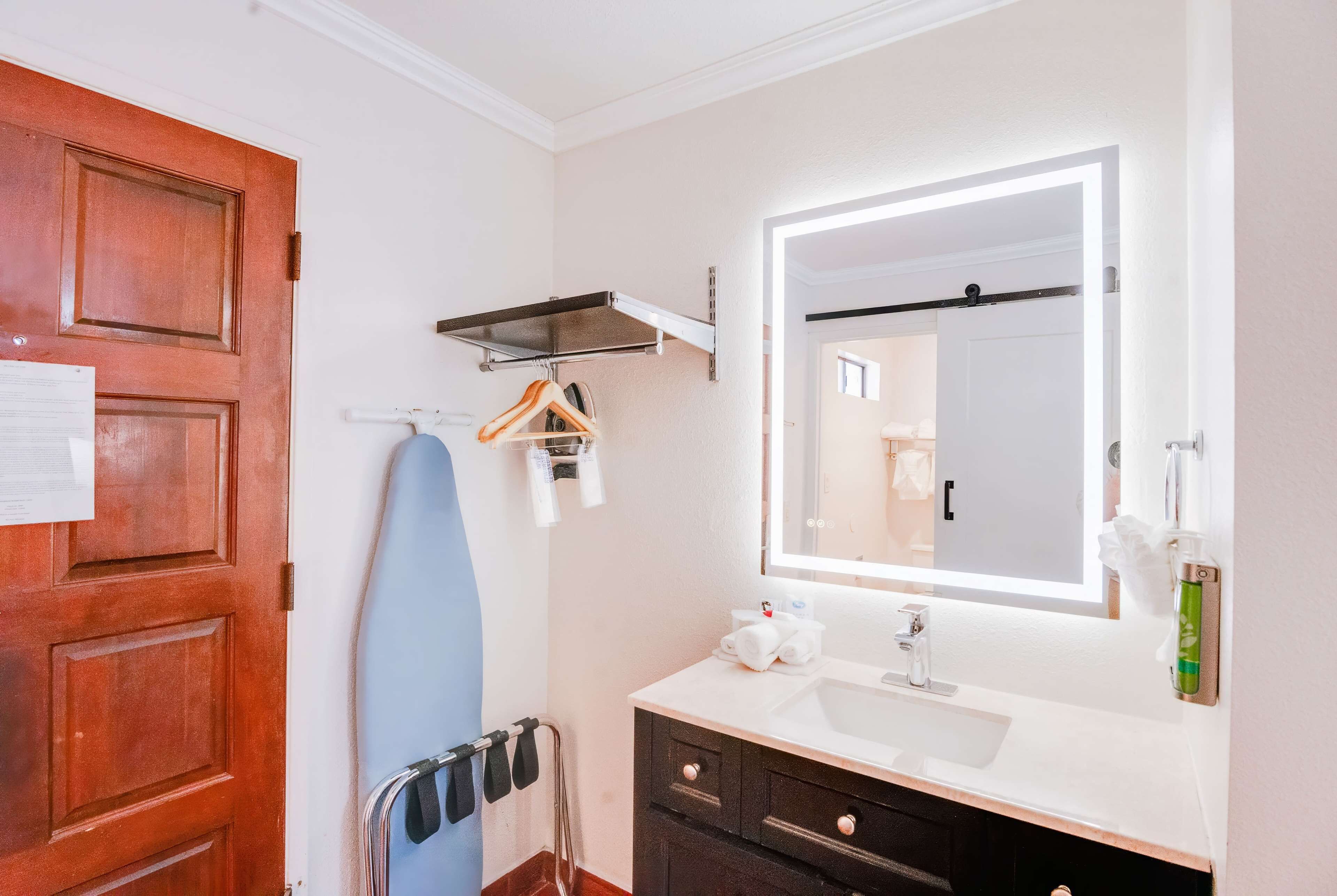 Un baño con puerta de madera, toallero, espejo, lavabo y dispensador de toallas.