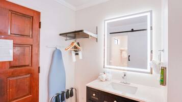 A bathroom with a wooden door, a towel rack, a mirror, a sink, and a towel dispenser.