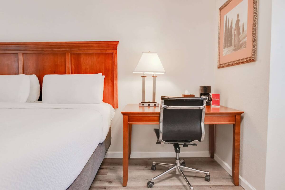 Ett hotellrum med en säng, ett skrivbord, en stol, en lampa och en inramad tavla på väggen.