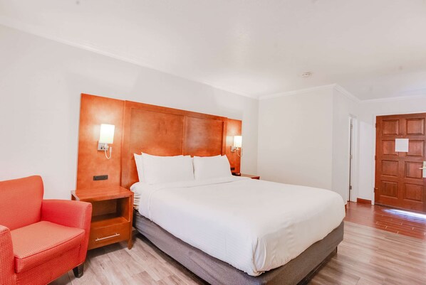 A hotel room with a large bed, a nightstand, a red chair, and a wooden door. - Ramada by Wyndham Mountain View (Mountain View)