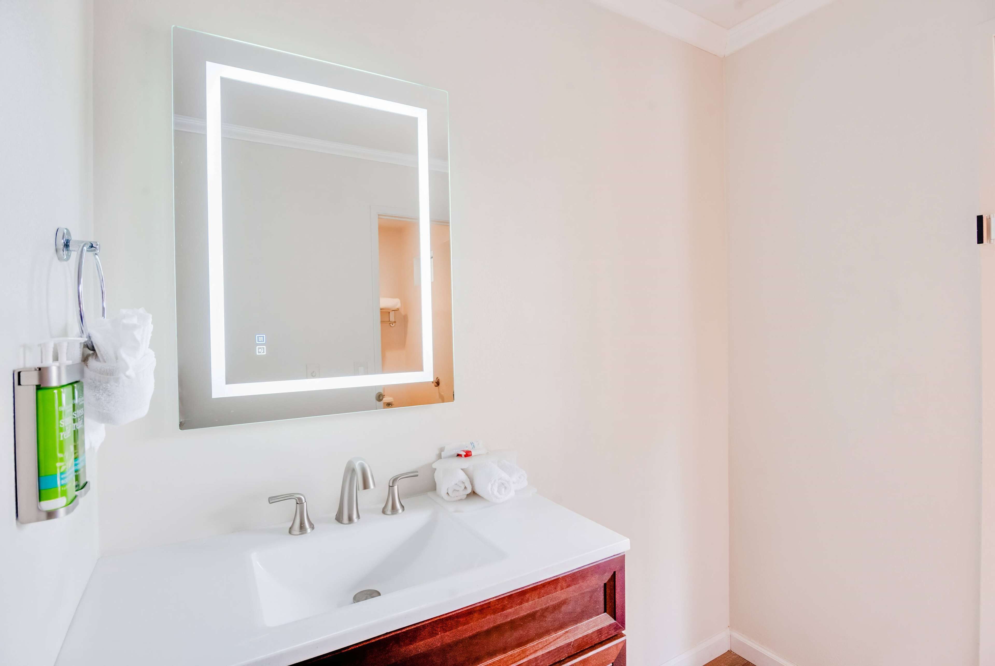 A bathroom with a white sink, a mirror with a light, and a towel dispenser.