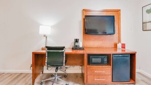A compact hotel room with a wooden desk, a black office chair, a flat-screen TV, a coffee maker, a microwave, and a mini fridge. - Ramada by Wyndham Mountain View (Mountain View)
