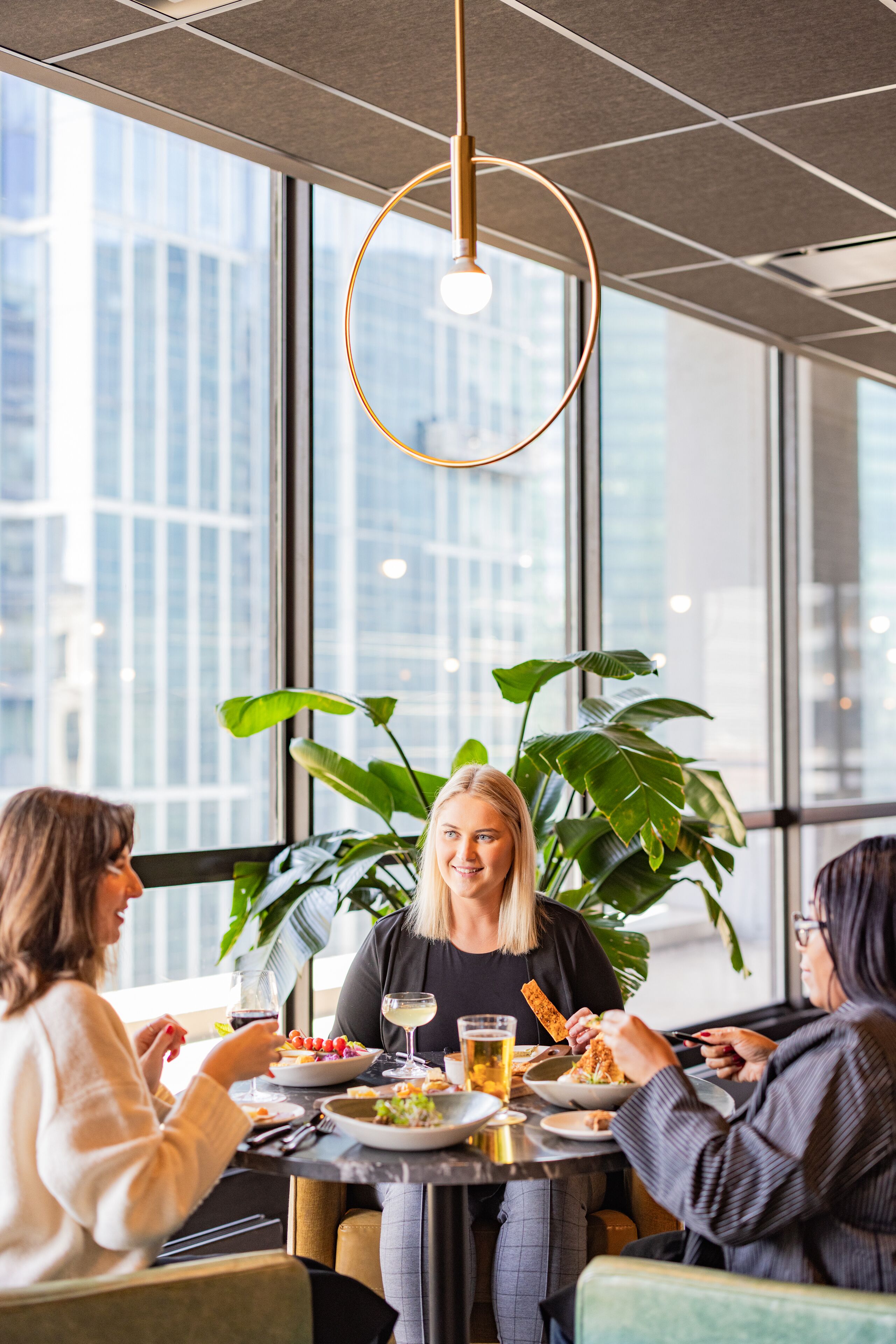 A modern dining area with large windows, a hanging light fixture, and indoor plants.