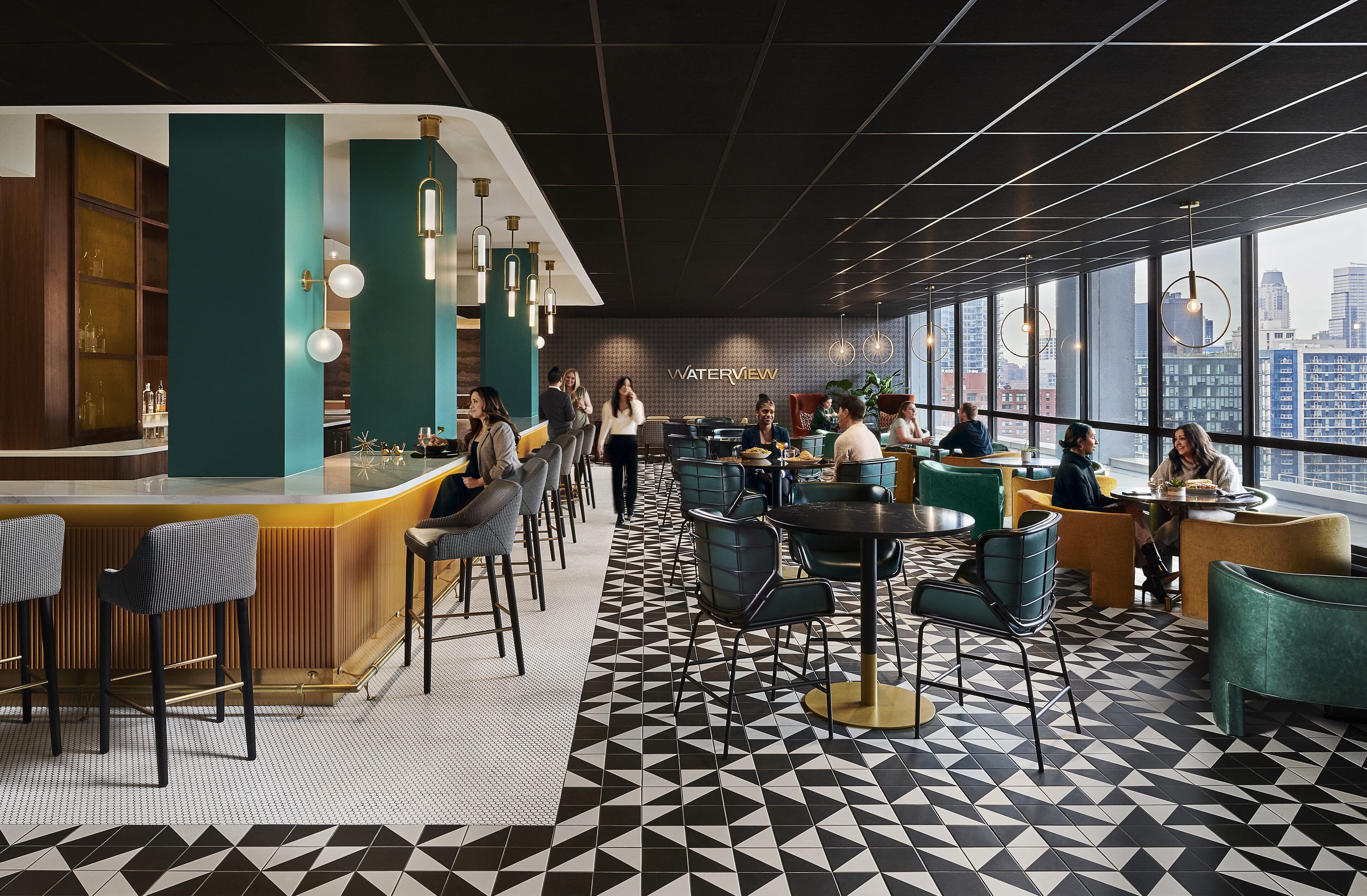 A modern bar area with a geometric patterned floor, bar stools, and a city view through large windows.