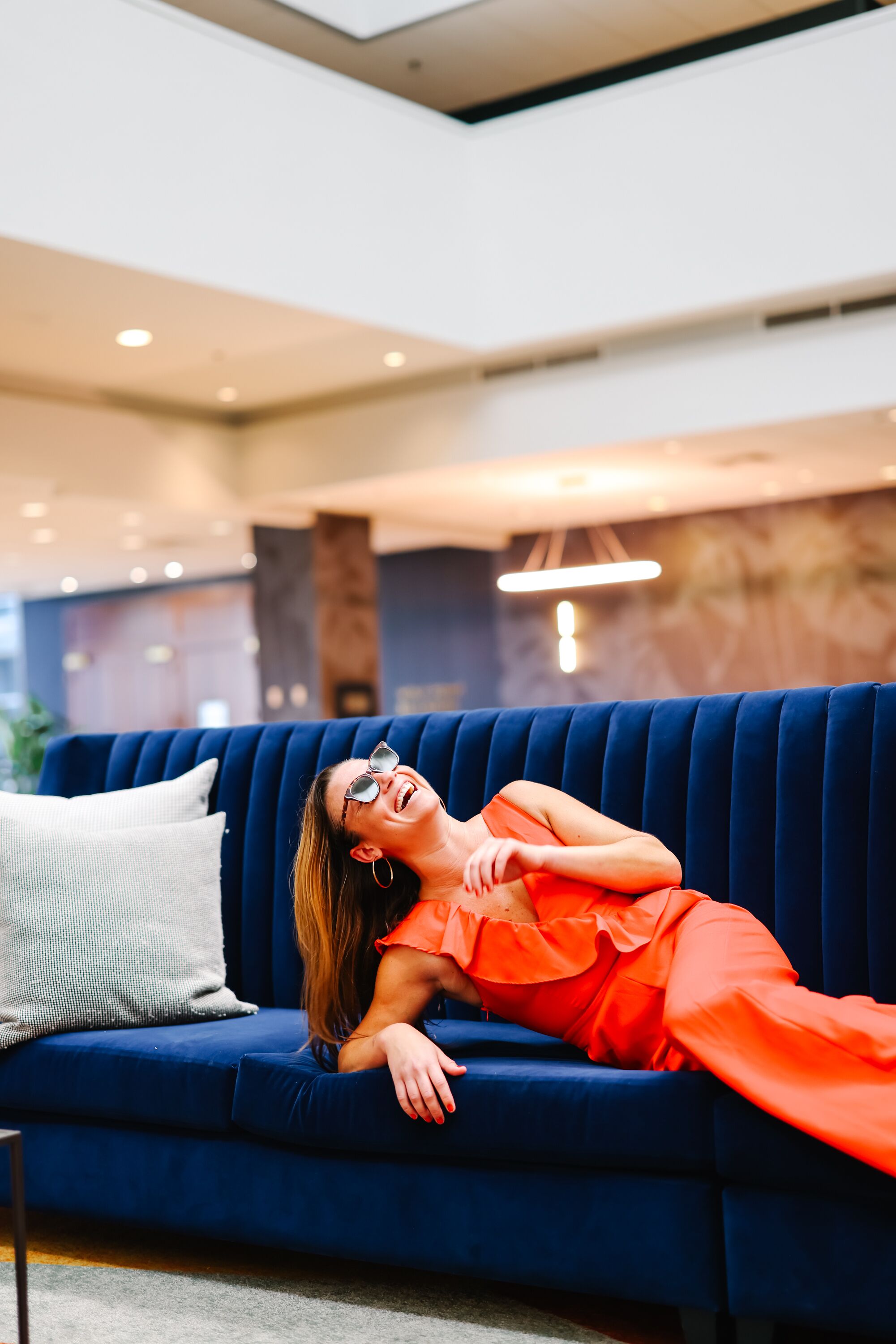 A person reclining on a blue sofa in a modern interior with a neutral-toned wall and recessed lighting.