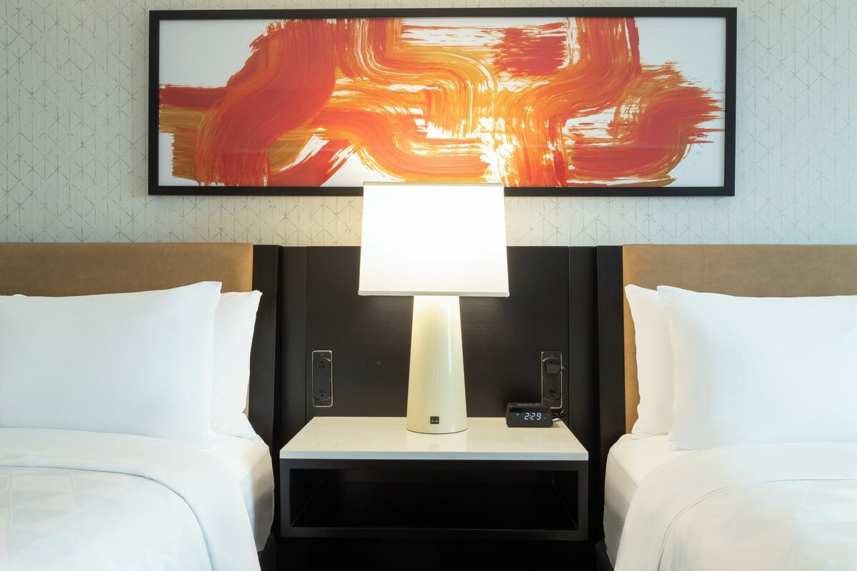 A hotel room with a bed, a bedside table with a lamp, and a digital clock.
