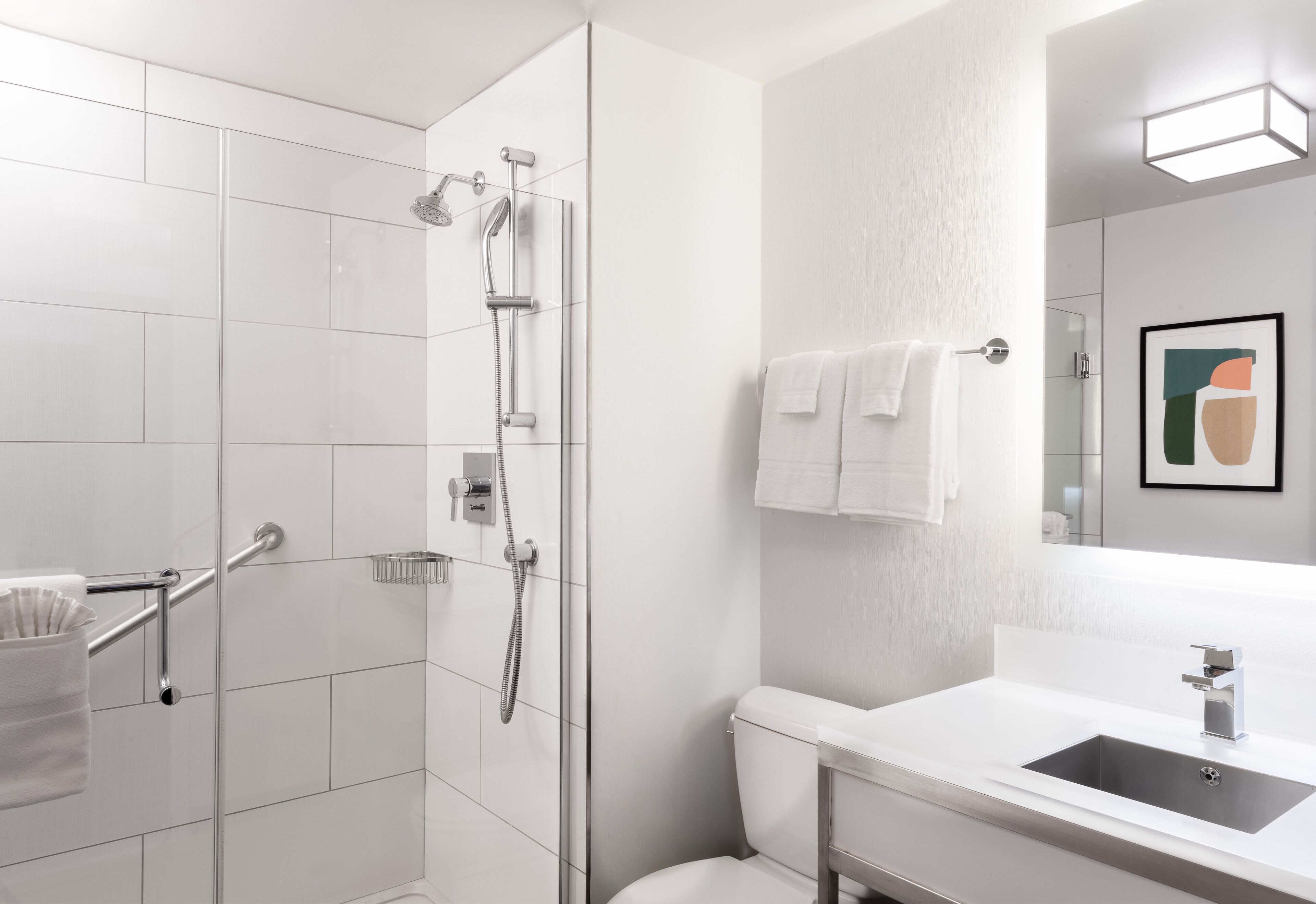 Een moderne badkamer met een douchecabine van glas, een witte wastafel en een toilet.