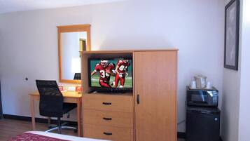 Habitación de hotel con cama, escritorio con computadora, televisor, espejo, microondas y refrigerador.