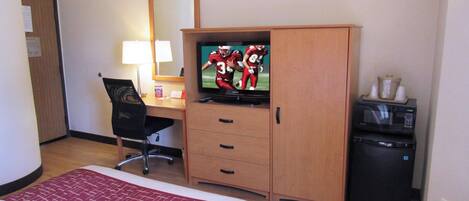 A hotel room with a bed, a desk with a chair, a television, a microwave, and a small trash bin.