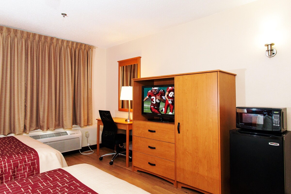 Habitación de hotel con cama, escritorio con silla, televisor, armario y refrigerador.