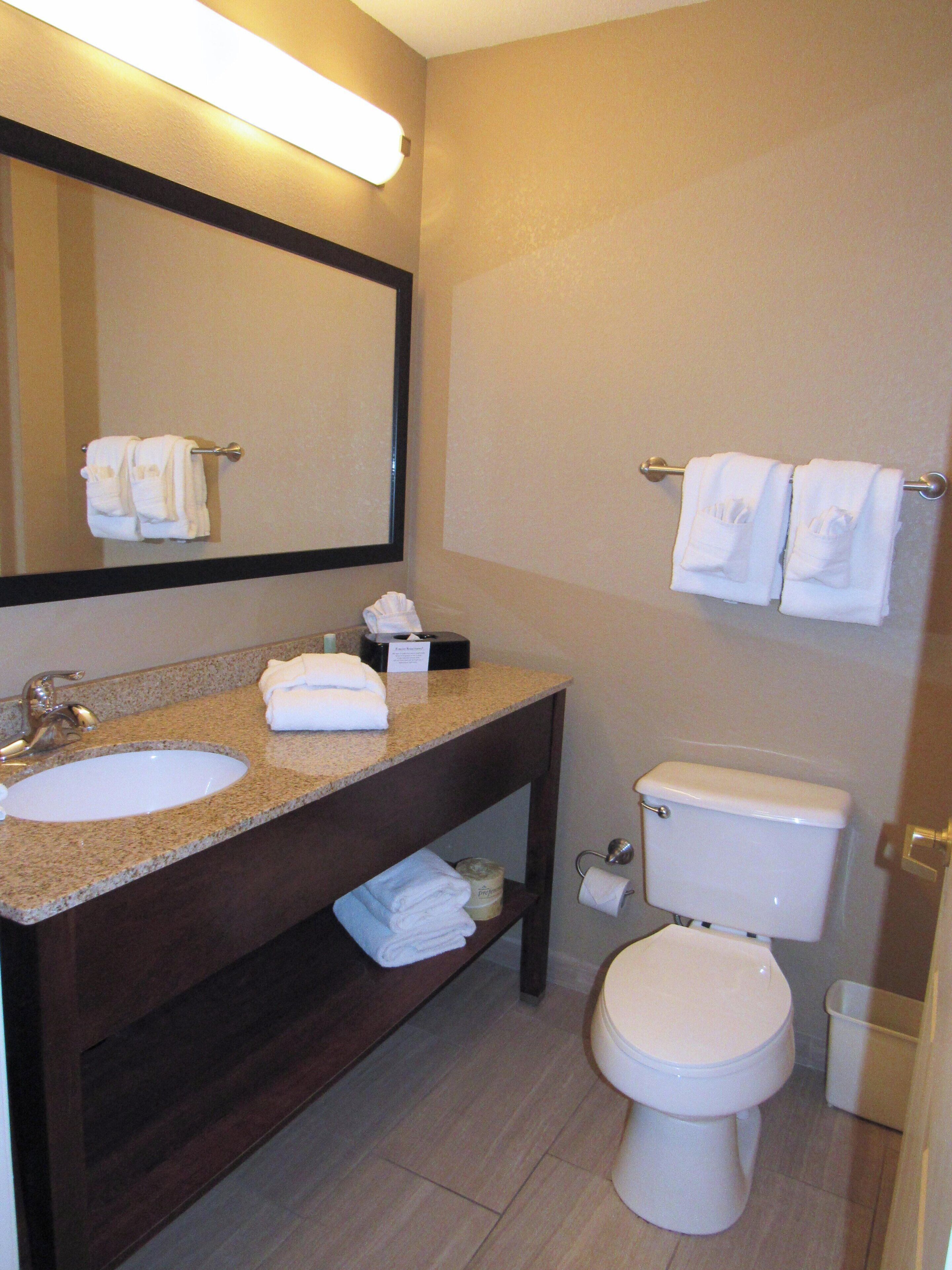 A bathroom with a sink, mirror, towel rack, toilet, and a trash bin.