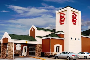 Un Red Roof Inn con una torre destacada, fachada de piedra y un estacionamiento con coches.