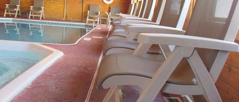 A row of white lounge chairs facing a pool, wooden walls, and a ceiling with exposed beams.