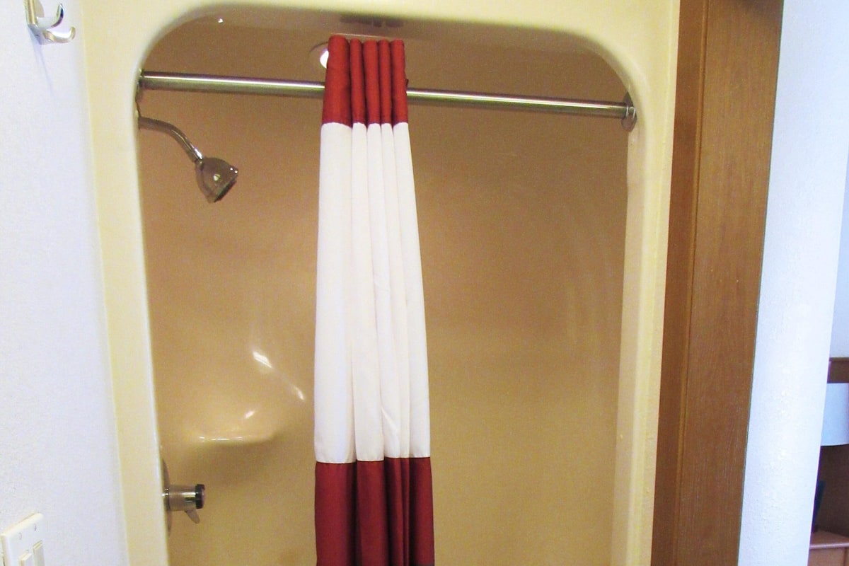 A shower area with a beige bathtub, a metal showerhead, and a white curtain with red and brown stripes.