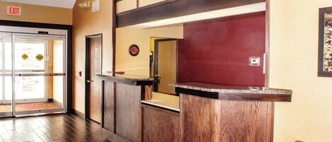 Zona de recepción con un mostrador de madera, puerta de cristal de entrada y un reloj en la pared.