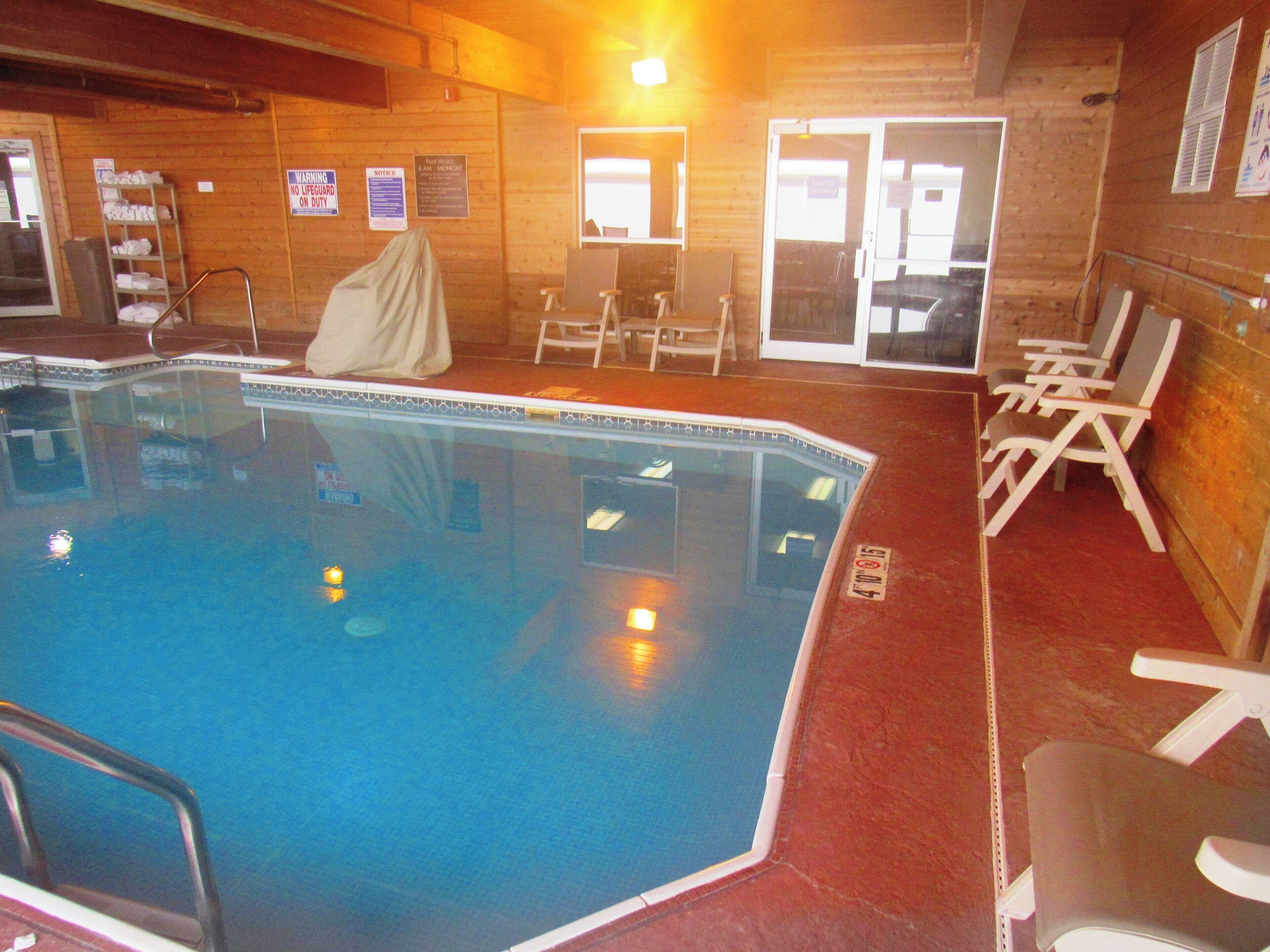 An indoor swimming pool with a tiled edge, surrounded by lounge chairs and a covered seating area.