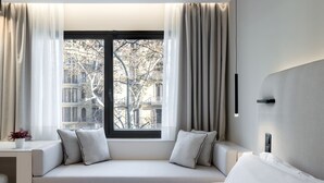 Moderni hotellihuone, jossa on suuri ikkuna, vuodesohva, yöpöytä ja sivupöytä.