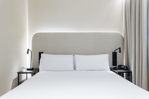 A hotel room with a large bed, two bedside tables, a lamp, a phone, and a cup on one table.