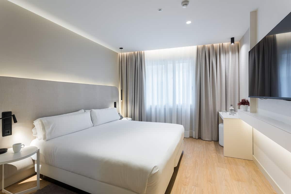 A modern hotel room with a large bed, bedside table, and a flat-screen TV mounted on the wall.