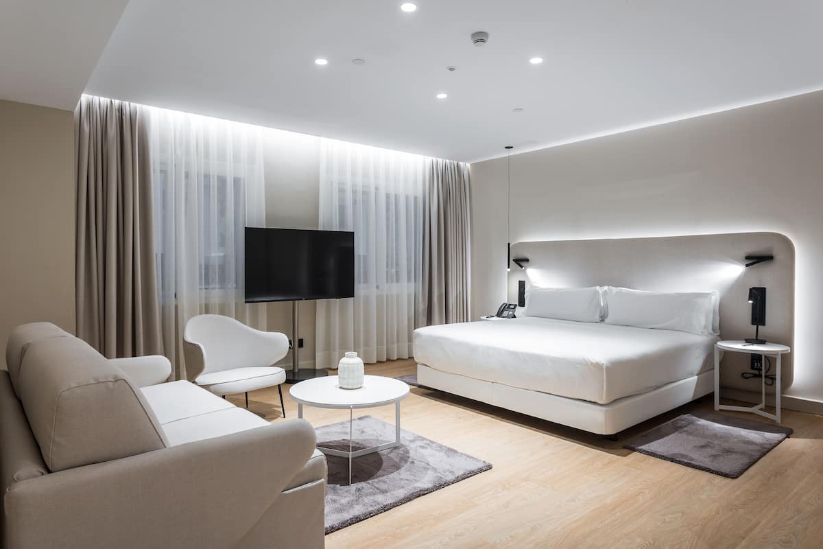 A modern hotel room with a large bed, a sofa, a TV, and a small table.