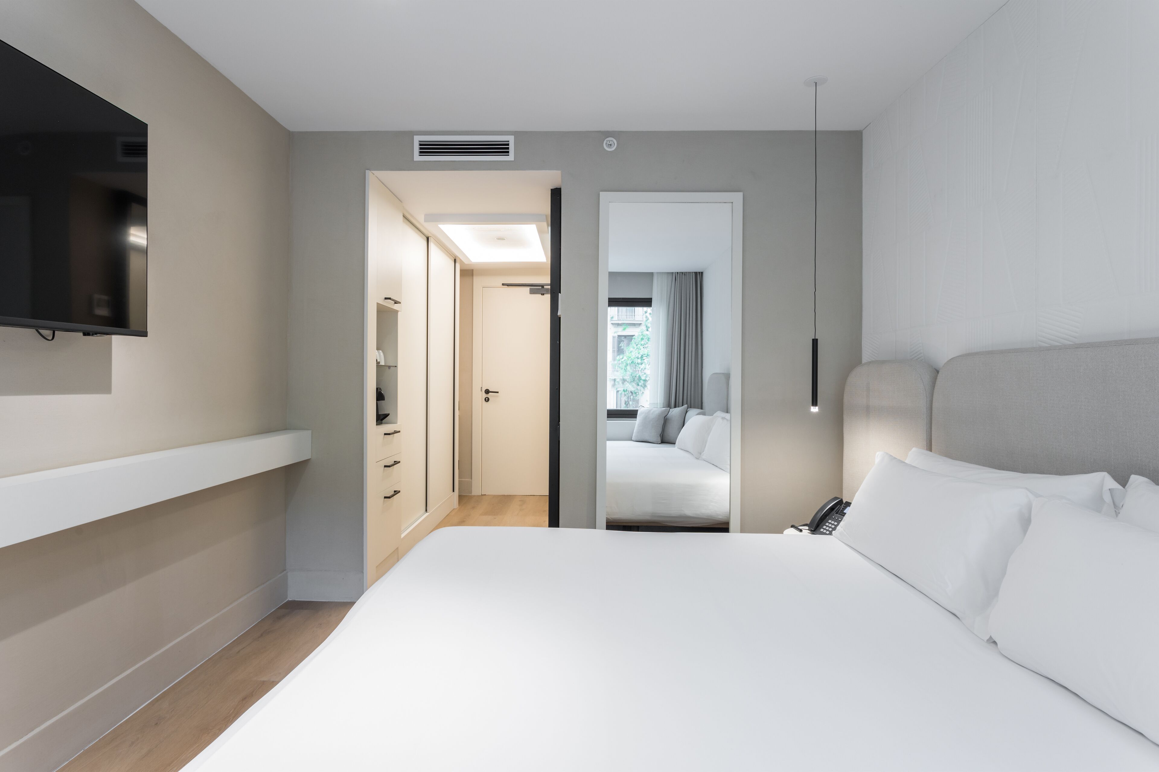 Une chambre d’hôtel moderne avec un grand lit, un téléviseur fixé au mur et un dressing.