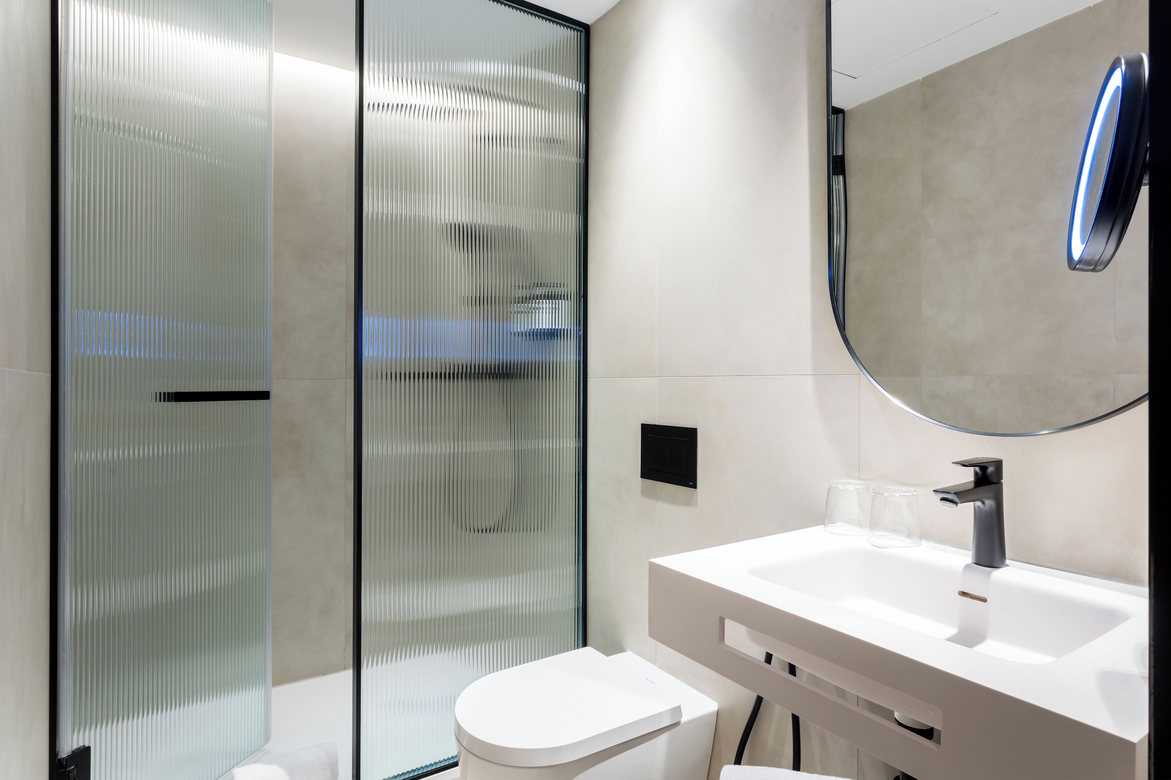 A modern bathroom with a white sink, a round mirror, and a toilet.