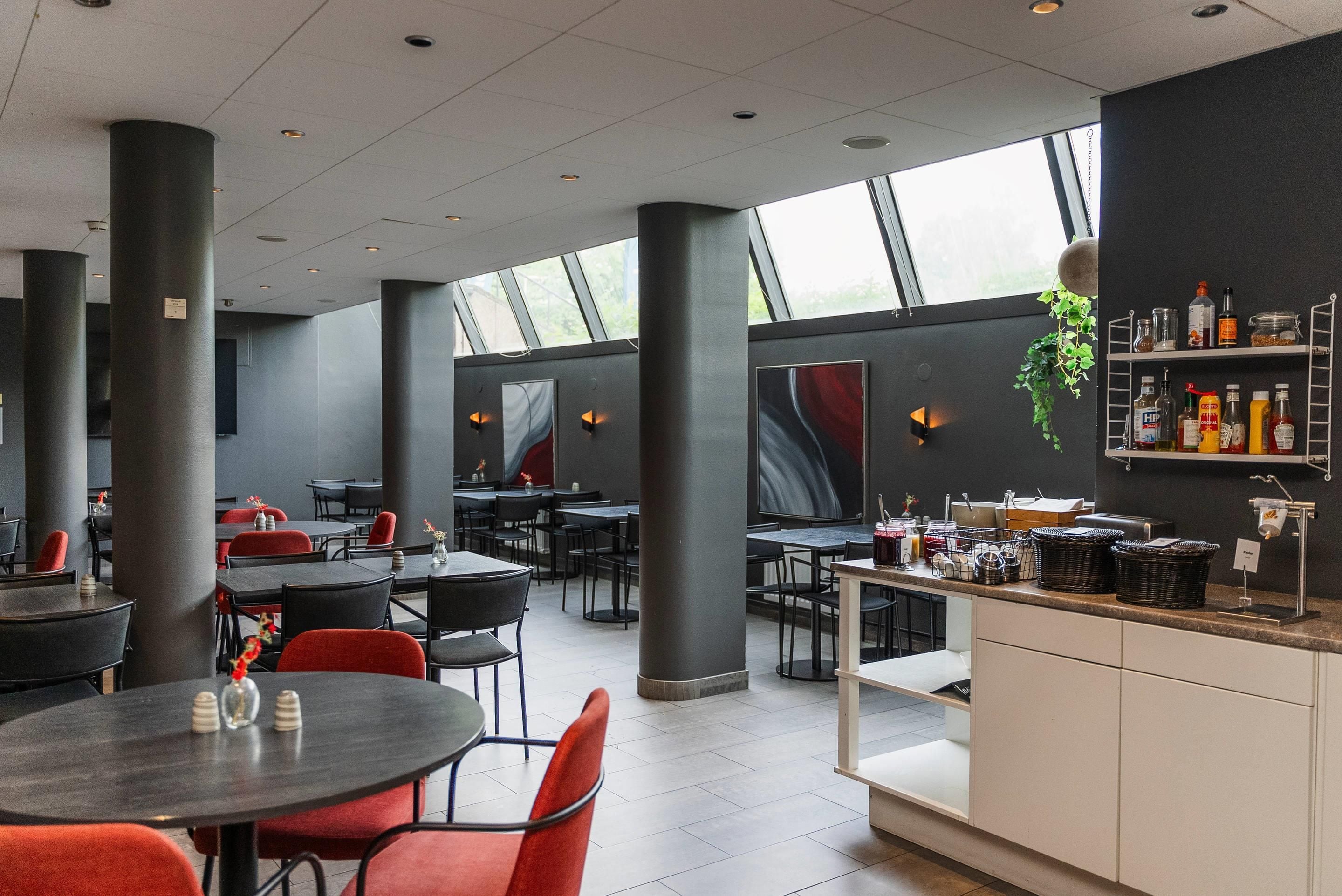 A modern restaurant interior with high ceilings, large windows, and a bar area with various bottles and a hanging plant.