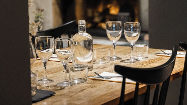 Une table à manger dressée avec des verres à vin et une bouteille, avec une cheminée en arrière-plan.