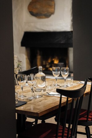 Una mesa de comedor dispuesta con copas de vino y una botella, con una chimenea al fondo.