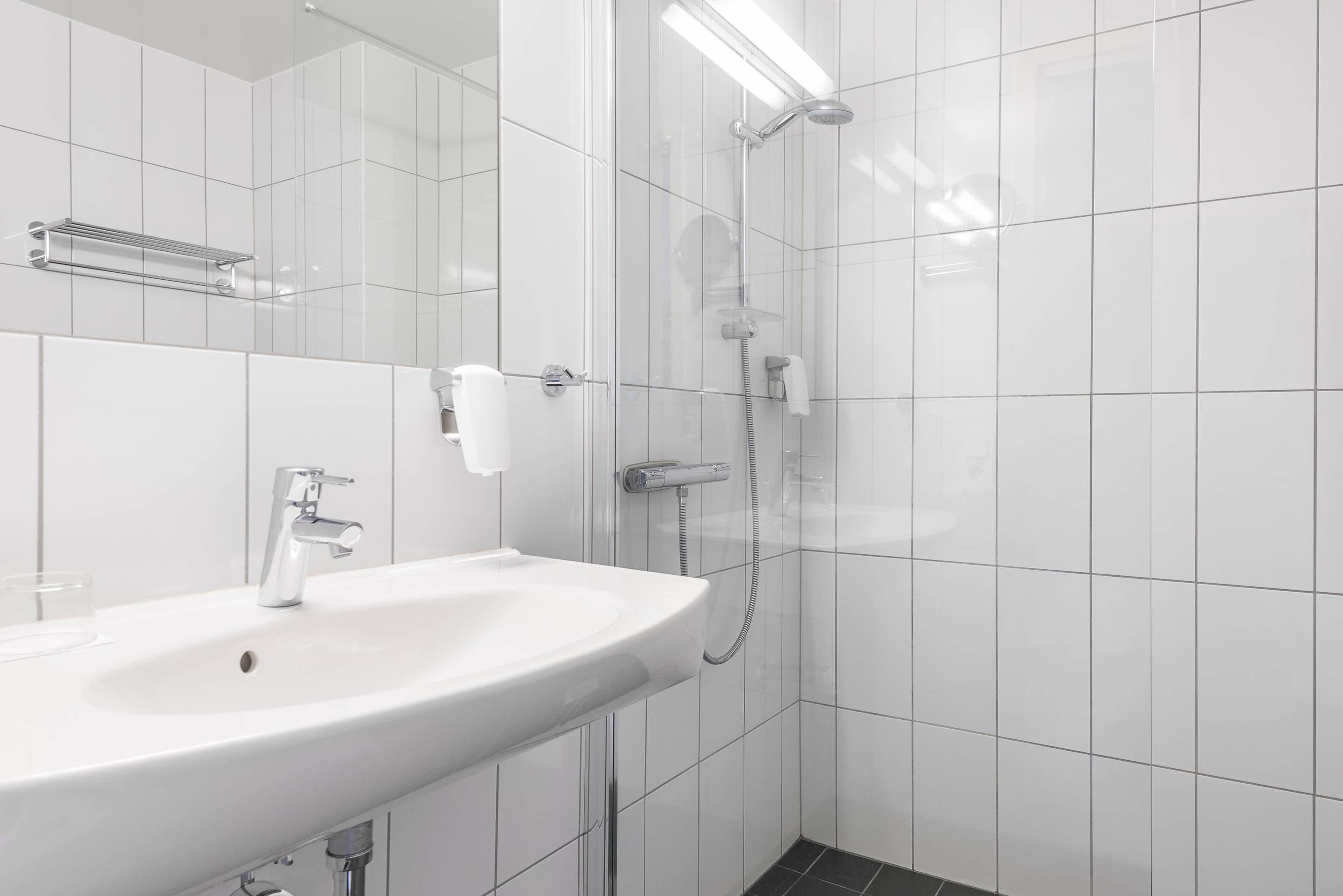 Un bagno moderno con un lavandino bianco, un soffione a mano e un portasciugamani.