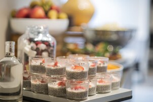 Una mesa de postres con vasitos de pudín de chía coronados con fresas, una botella y un bol de frutas al fondo.