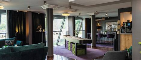 A modern living room with a pool table, a green sofa, and a bar area with seating.