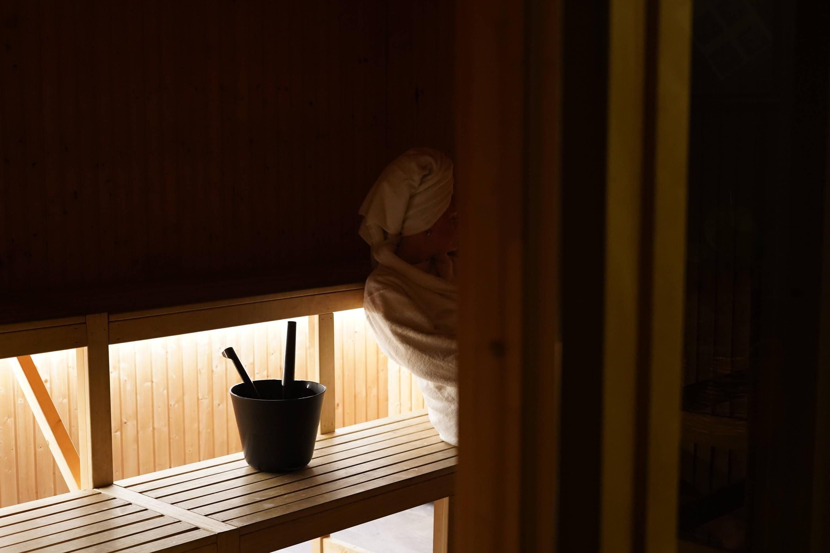 A wooden bench with a black bucket and a spoon, a towel hanging on the wall, and a wooden door frame.