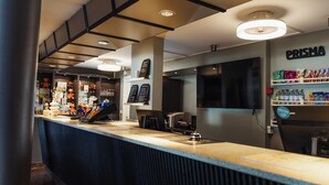 Un espace bar moderne avec un comptoir, des étagères remplies de collations, un téléviseur et un panneau indiquant « PRISMA ».