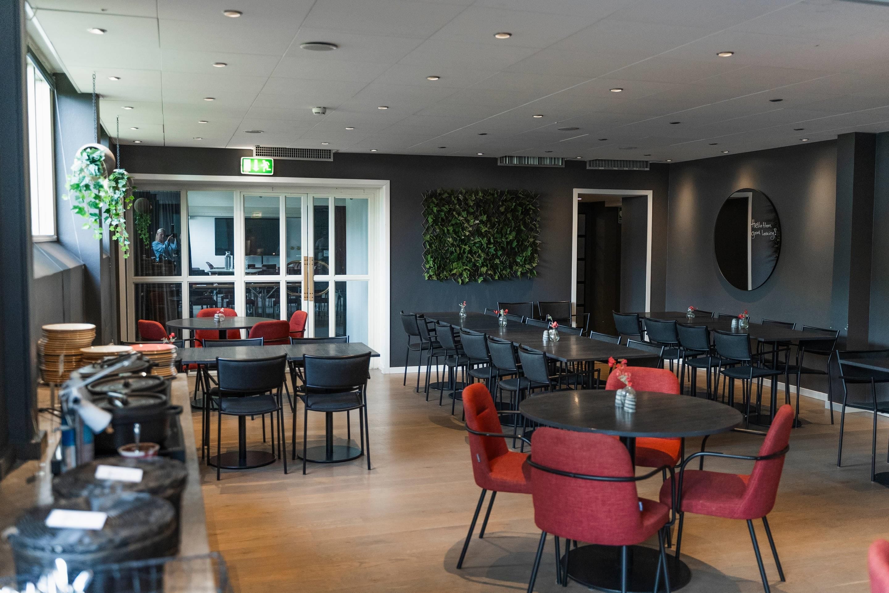 A modern dining area with multiple tables and chairs, a large window, and a green wall decoration.