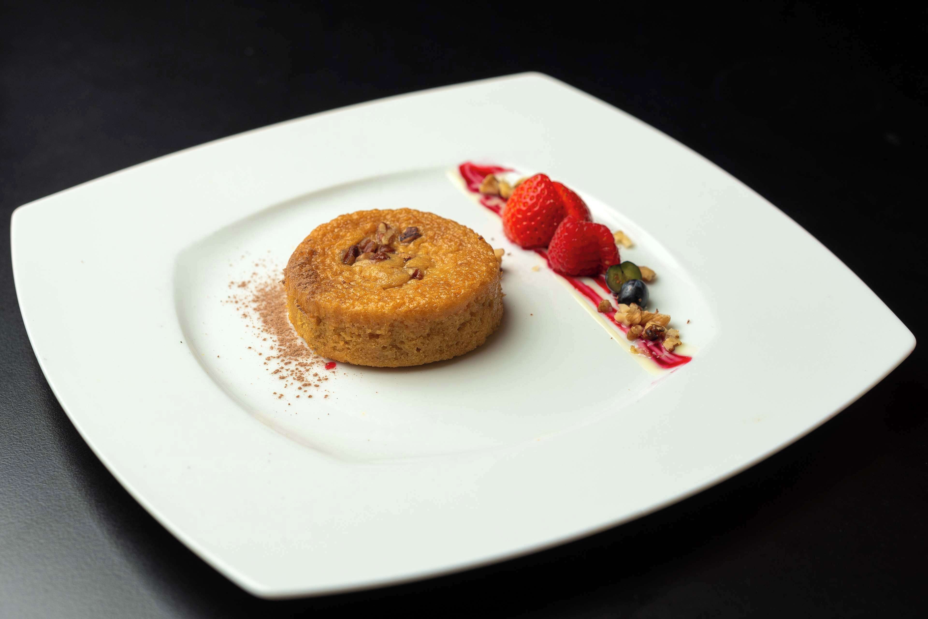 A dessert on a white plate with strawberries and a dusting of cocoa powder.