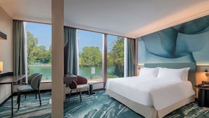 Ein Hotelzimmer mit einem großen Bett, einem Schreibtisch, einem Stuhl und Blick auf einen See.