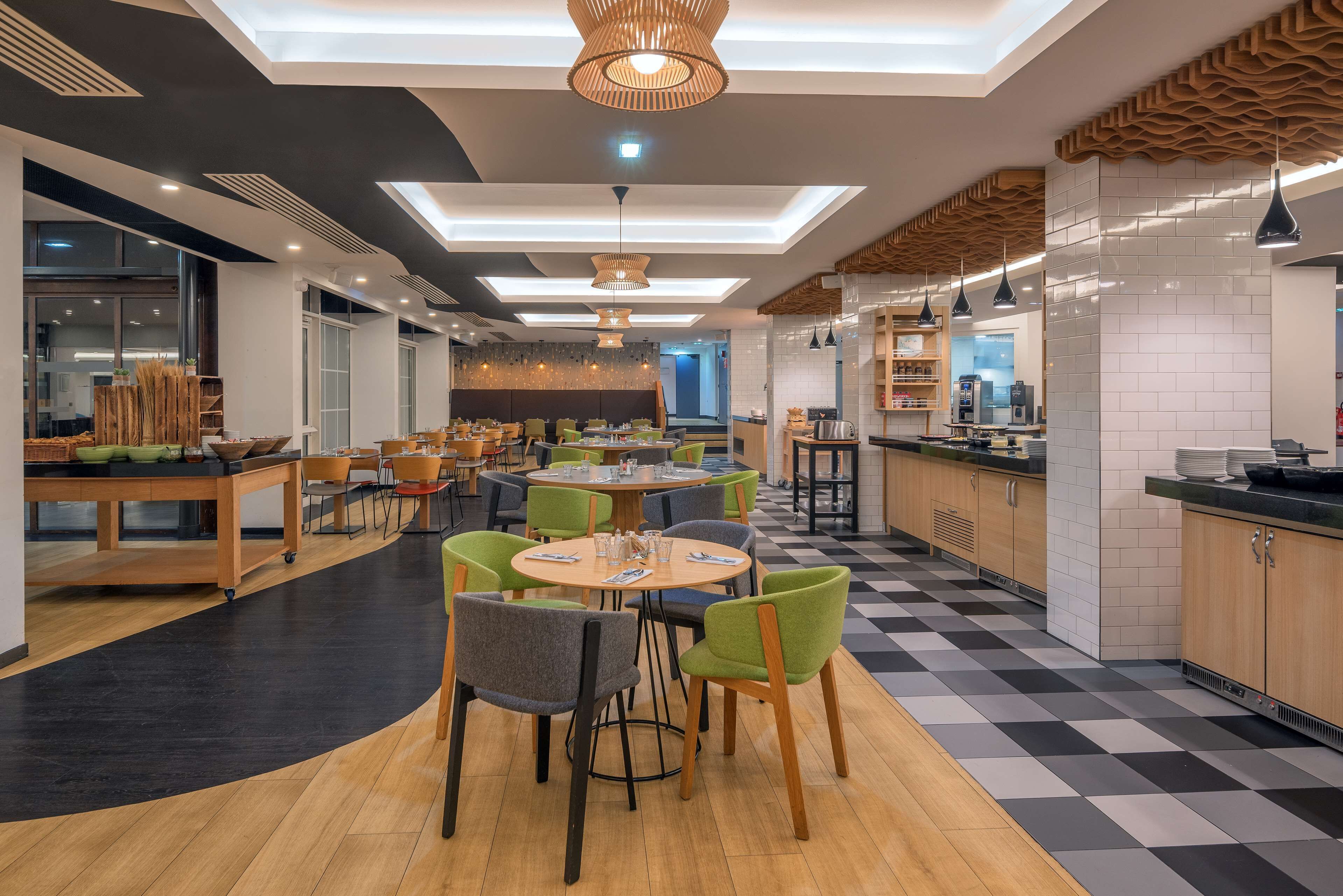 A modern restaurant with round tables, green and gray chairs, and a checkered floor.