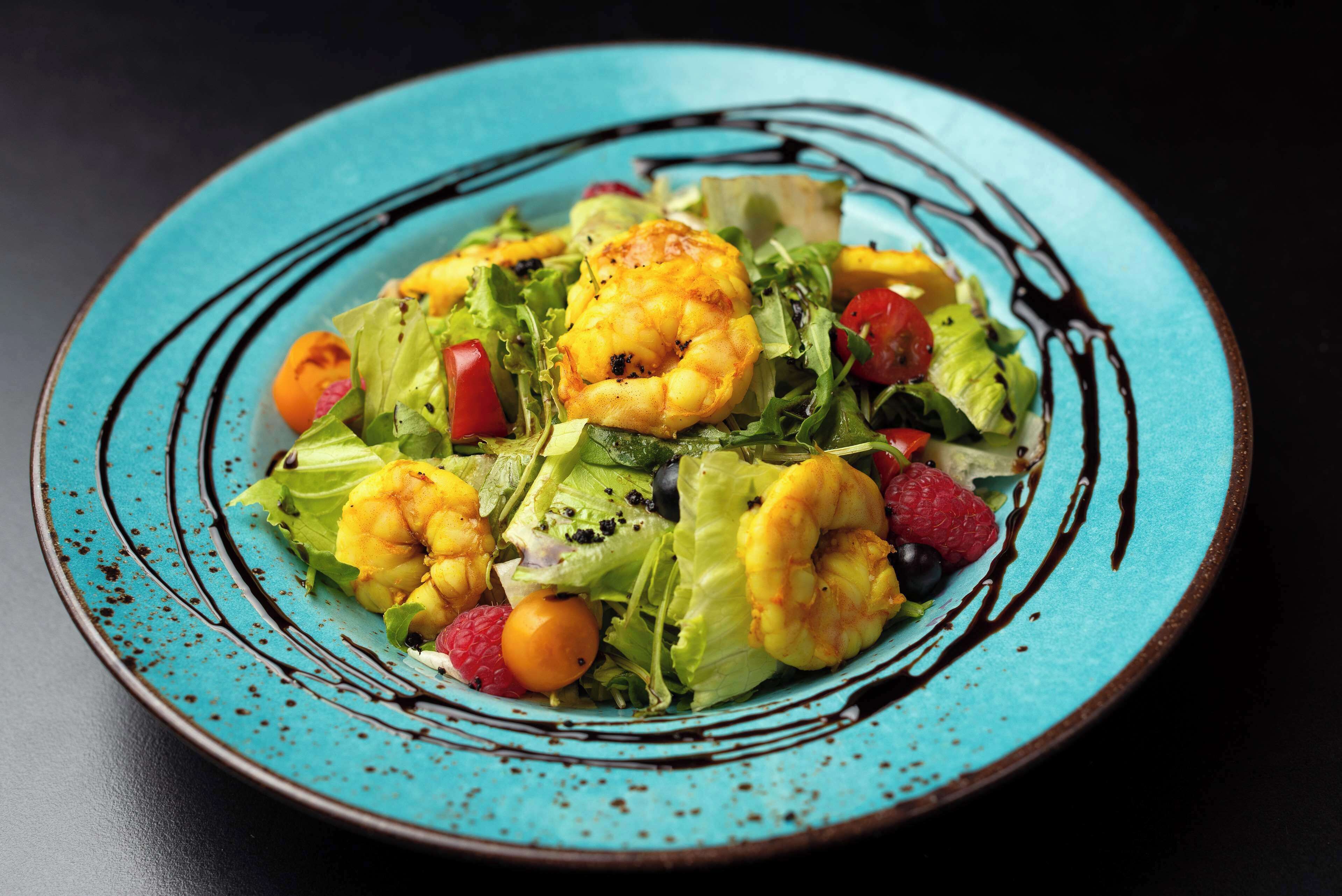 A plate of shrimp and salad with a blue rim.