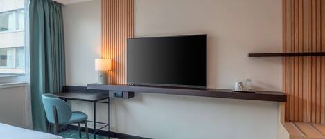 Una habitación de hotel con una cama, un escritorio con silla, un televisor y una lámpara.