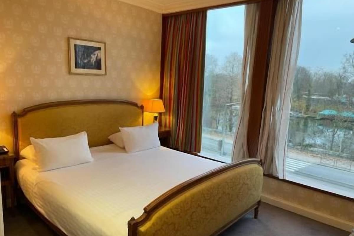 A hotel room with a large bed, a nightstand, a lamp, and a window with curtains.
