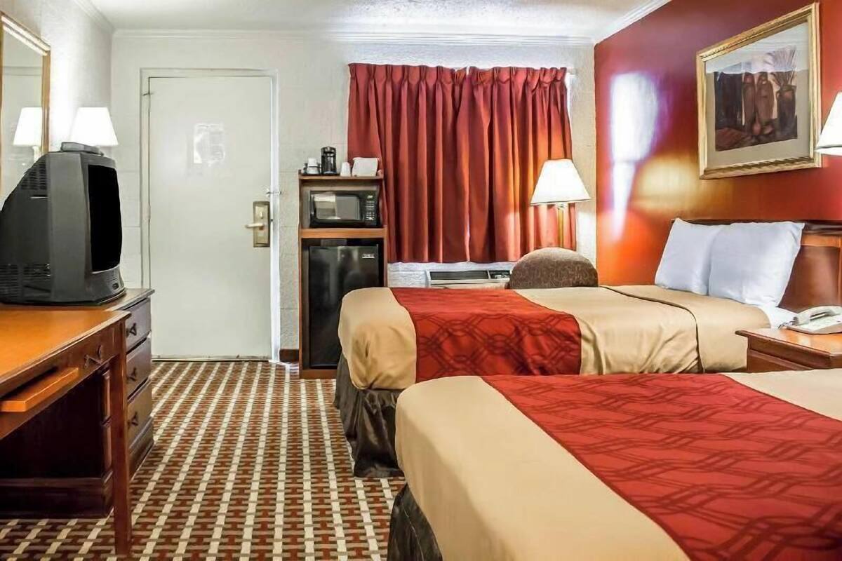 A hotel room with two beds, a television, a microwave, a desk, and a door.