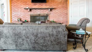 Una sala de estar con chimenea de ladrillo, un sofá, un sillón y una mesita con una caja de pañuelos.