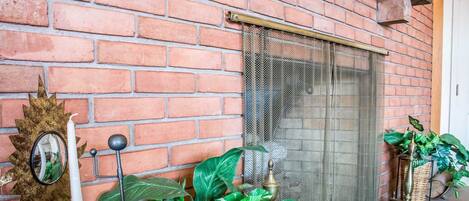 Un muro de ladrillo con una puerta metálica mosquitera, un espejo decorativo y plantas en macetas.