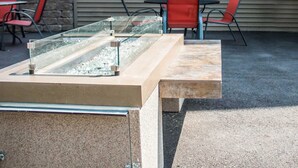 Un área de estar al aire libre con una mesa de vidrio y sillas, un banco de piedra y un muro de piedra de fondo.