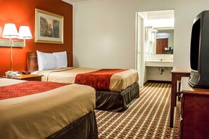 Habitación de hotel con dos camas, un escritorio con lámpara, televisión y baño visible a través de una puerta abierta.