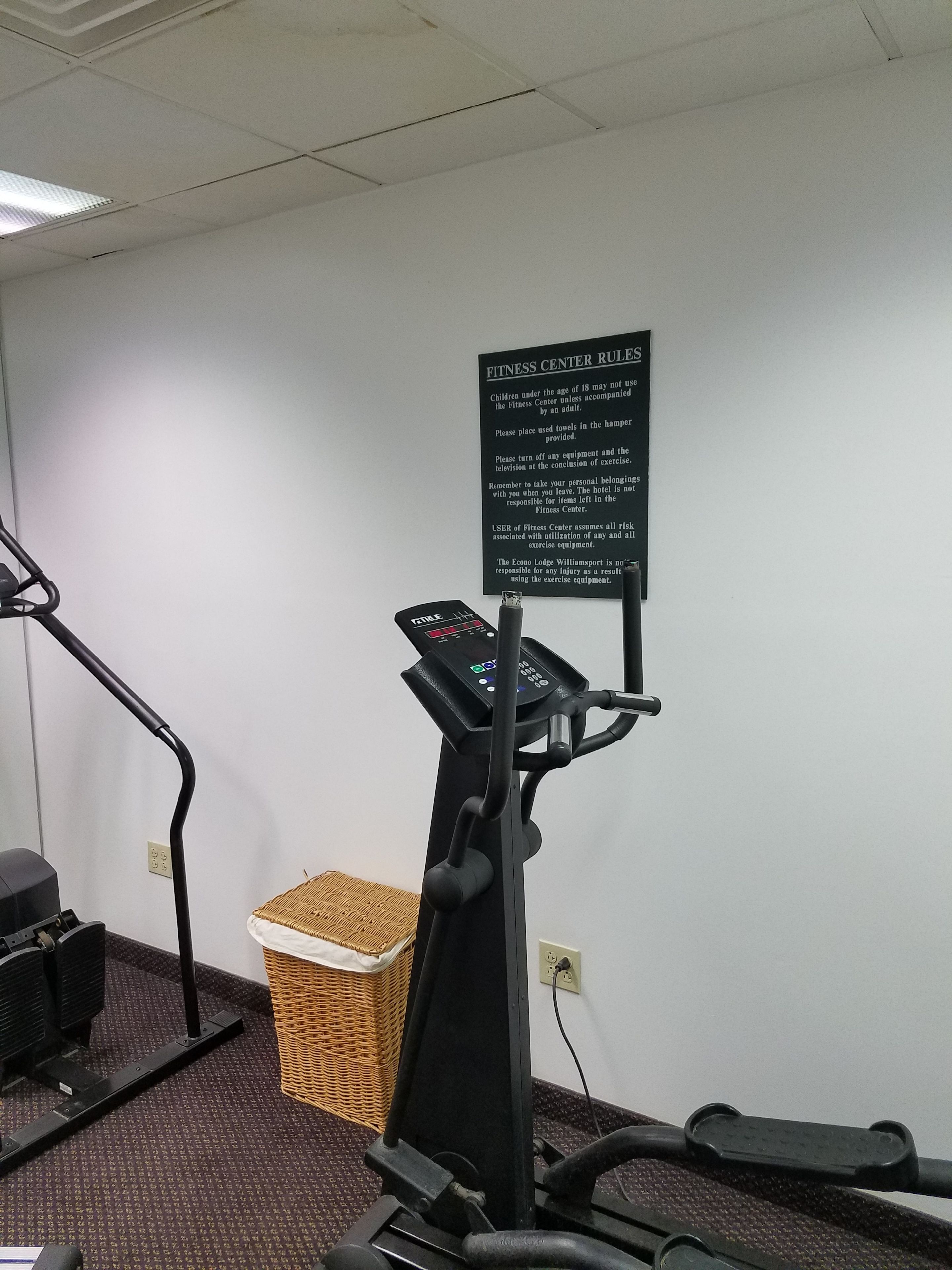 A fitness center with exercise equipment, a wall-mounted sign with rules, and a wicker basket.