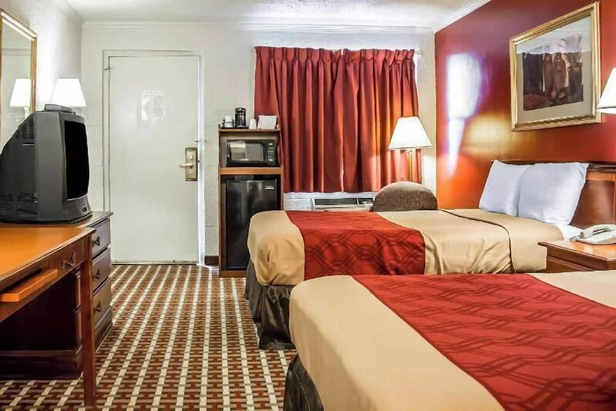 Una habitación de hotel con dos camas, televisión, microondas, escritorio y una puerta.