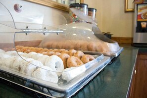Un bufé con diversas pastelerías y postres exhibidos en una zona de servicio cubierta con vidrio.
